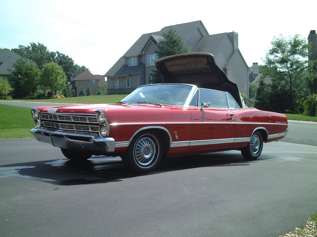 Red vintage Ford convertible parked in driveway, front three-quarter view