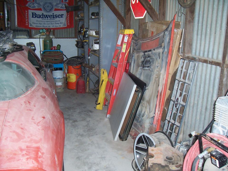 red car body in garage, parts leaning against wall, ladder, Budweiser flag