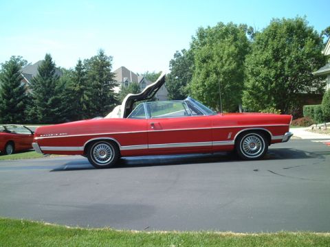 1967 Ford Galaxie - Red 1967 Ford Galaxie convertible with top partially up, parked outside.