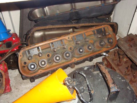 1989 Ford Bronco - Several rusty engine cylinder heads are piled together with other engine components and a yellow funnel in a storage area.