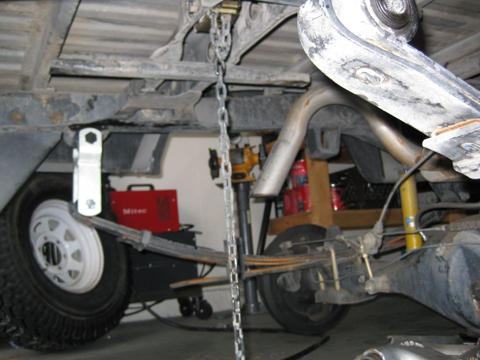 Under-truck view of rear leaf springs, yellow shock, axle and exhaust over axle in garage