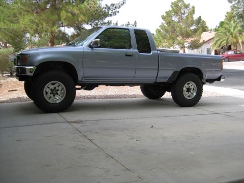 1990 Toyota Pickup/SR5 - A lifted Toyota pickup truck is parked on a concrete driveway with trees in the background.