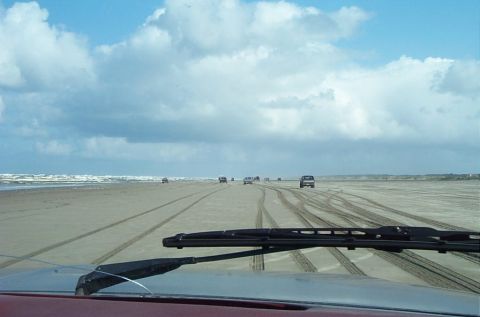 1989 Ford F-150 - Several vehicles drive along a wide, sandy beach under a cloudy sky.