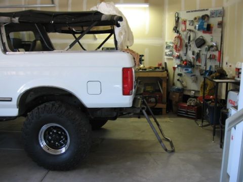 1995 Ford Bronco - Rear view of a white Ford Bronco with a custom tire carrier, parked indoors.