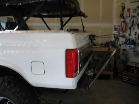 1995 Ford Bronco - Rear view of a white 1995 Ford Bronco a drop-down tire carrier and a soft top.