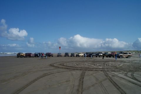 1989 Ford F-150 - A group of vehicles are parked on a sandy beach under a blue sky with scattered clouds.
