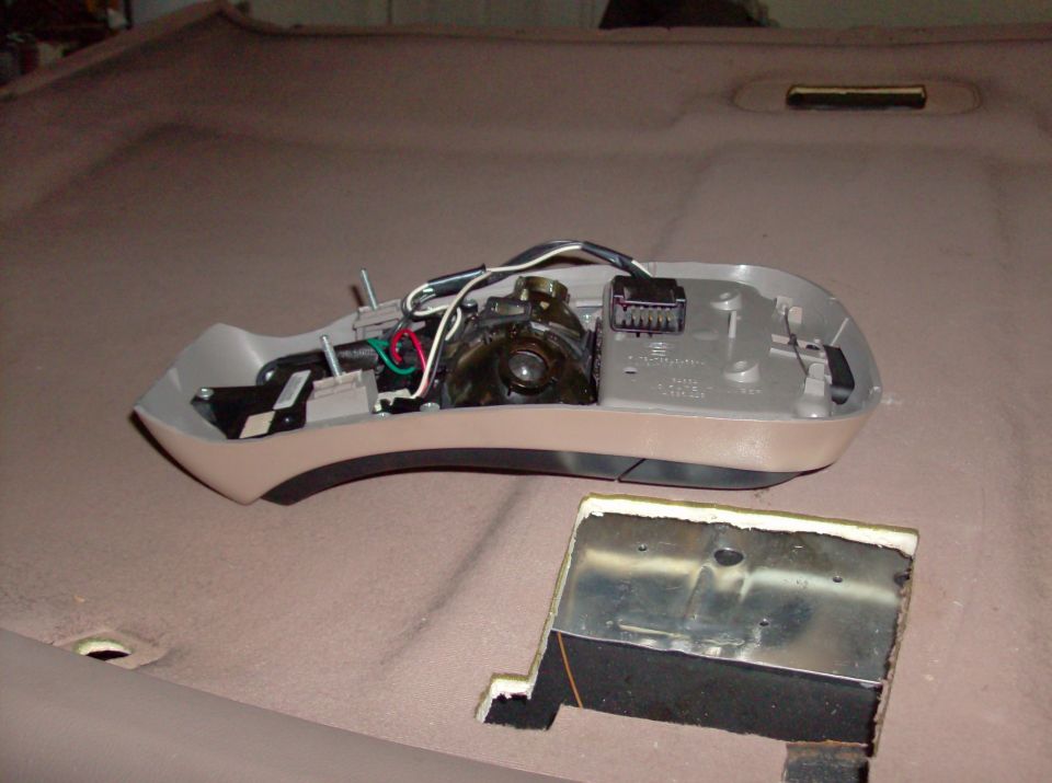 Removed overhead dome light console showing wiring on a tan headliner with mounting cutout below