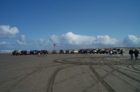 1989 Ford F-150 - Several vehicles are parked on the sand near the ocean under a partly cloudy sky.