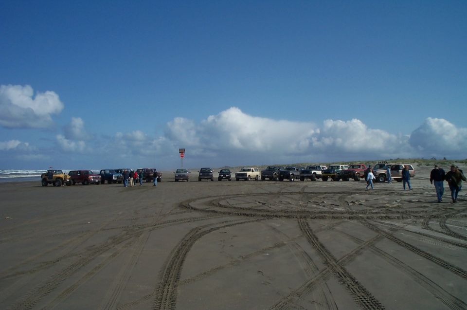 Long row of 4x4 Jeeps, pickups and SUVs parked on a beach with tire tracks in the sand