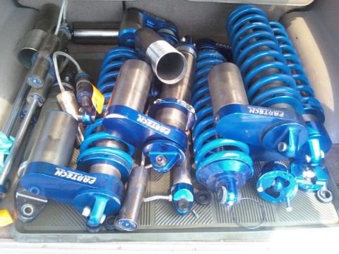 1984 Ford Bronco - Several blue coilover shock absorbers are piled up, some with visible branding.