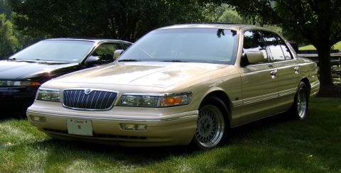 1996 Mercury Grand Marquis - 1996 Mercury Grand Marquis in tan, parked on a lawn with a dark sedan behind it.