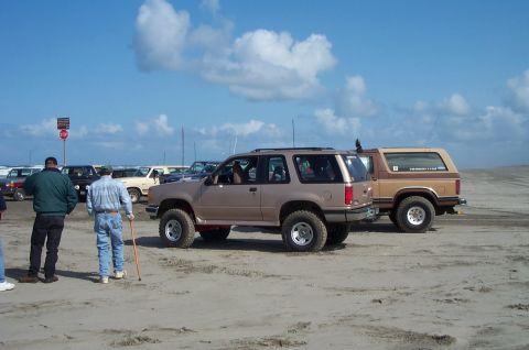 1989 Ford F-150 - Two SUVs are parked on a sandy beach under a partly cloudy sky.