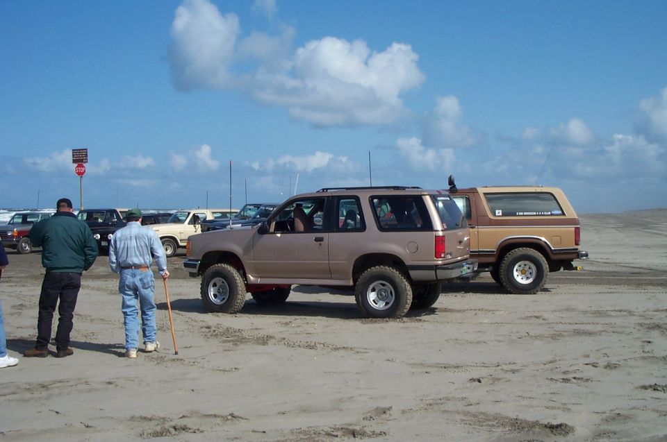 Lifted tan Ford Explorer parked on beach sand next to a two-tone brown Ford Bronco