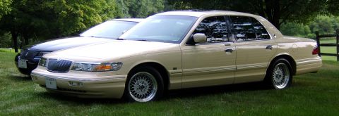 1996 Mercury Grand Marquis - A tan 1995 Mercury Grand Marquis sedan is parked on a grassy lawn next to a dark-colored sedan.