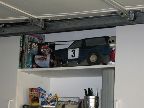 1986 Ford Bronco - A toy car with racing decals sits on a shelf among other collectibles and books.