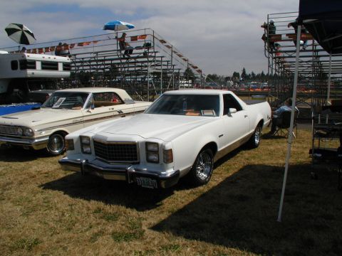 1967 Ford Ranchero - A white pickup truck is parked on a grassy field with bleachers and other vehicles visible.