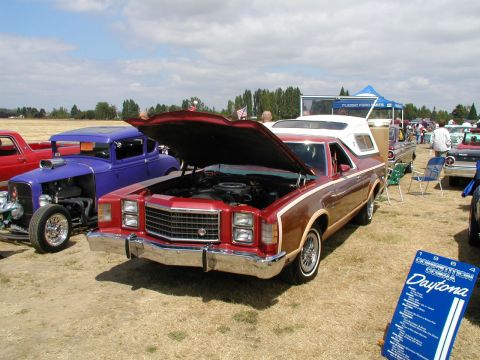 1967 Ford Ranchero - A red pickup truck with wood paneling is displayed with its hood open at an outdoor car show.
