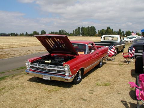 1967 Ford Ranchero - A red 1967 Ford Ranchero is displayed with its hood open at a car show, with other vehicles and American flag-themed chairs nearby.