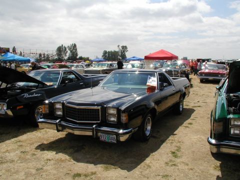 1967 Ford Ranchero - A black Ford Ranchero is displayed at an outdoor car show with other vehicles and tents in the background.
