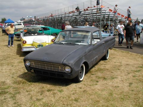 1967 Ford Ranchero - A matte gray pickup truck sits on a grassy field with spectators and other vehicles in the background.
