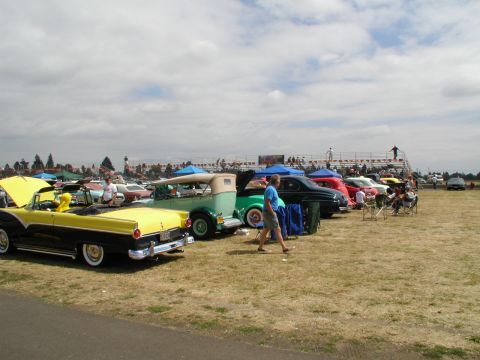 1967 Ford Ranchero - A car show features several classic vehicles on a sunny day with spectators in the background.