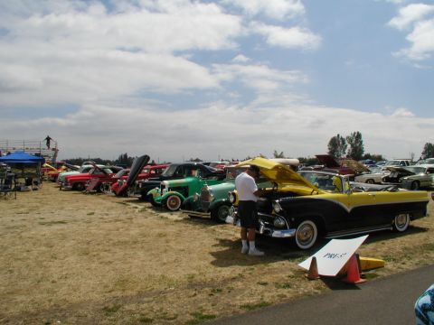 1967 Ford Ranchero - A two-tone yellow and black convertible is displayed with its hood open at a car show, alongside other classic vehicles.