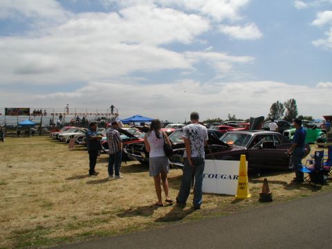 1967 Ford Ranchero - Attendees examine vehicles at an outdoor car show, with bleachers and tents visible in the background.