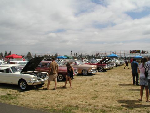 1967 Ford Ranchero - A line of classic cars are parked on a grassy field under a cloudy sky at an outdoor event.
