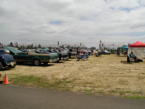 1967 Ford Ranchero - Several vehicles are on display at an outdoor event with spectators and tents in the background under a cloudy sky.