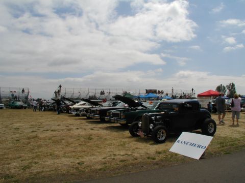 1967 Ford Ranchero - A line of cars are displayed at an outdoor event, with a black hot rod in the foreground.