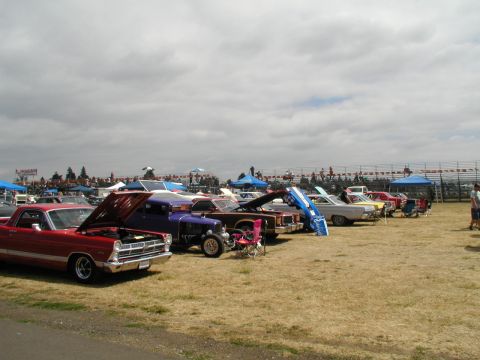 1967 Ford Ranchero - Several classic vehicles are displayed on a dry grass field under a cloudy sky, with spectators in the background.
