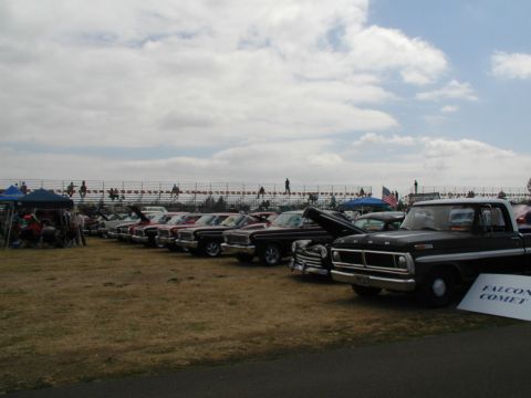 1967 Ford Ranchero - A row of classic Ford trucks and cars are displayed at a show under a cloudy sky.