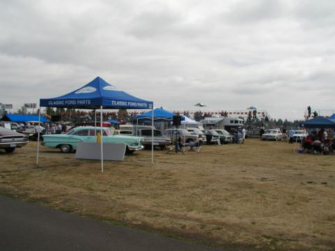 1967 Ford Ranchero - An outdoor event with multiple vehicles displayed under tents, with spectators in the background.