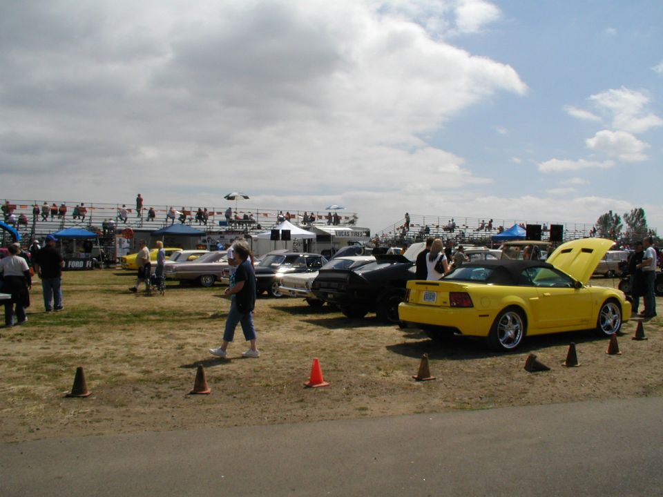 Yellow convertible sports car with hood open, parked next to other cars at an outdoor event