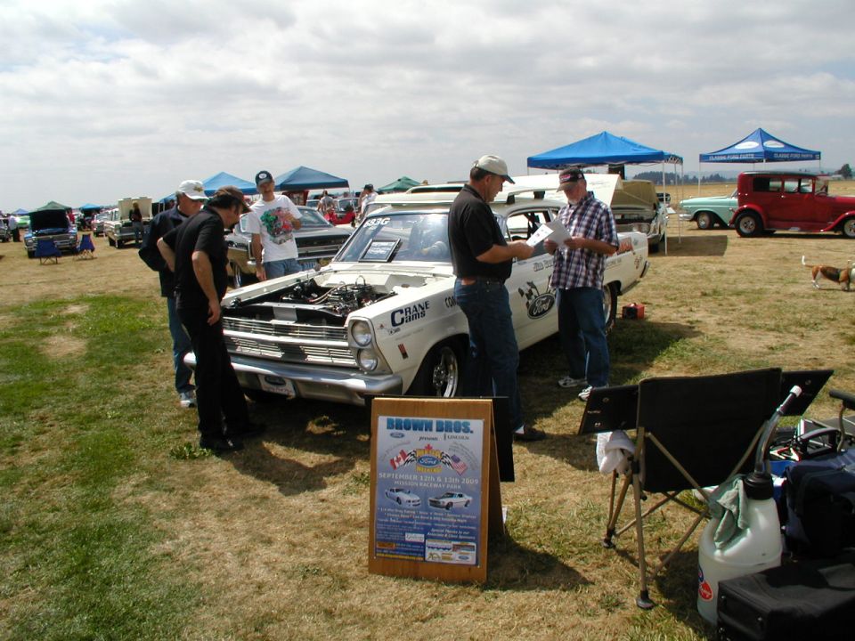 1967 Ford Ranchero with hood open, people gathered around, at a car show. Sign in foreground