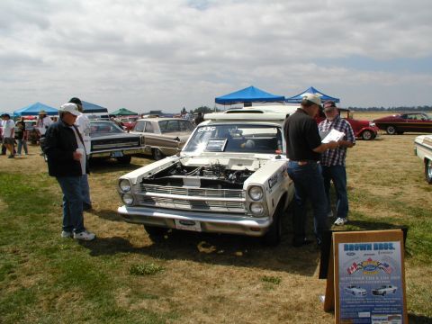 1967 Ford Ranchero - A white 1965 Ford Fairlane is displayed with its hood up at an outdoor car show.