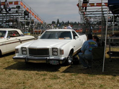 1967 Ford Ranchero - A white pickup truck with a bed is parked on grass near bleachers at an outdoor event.