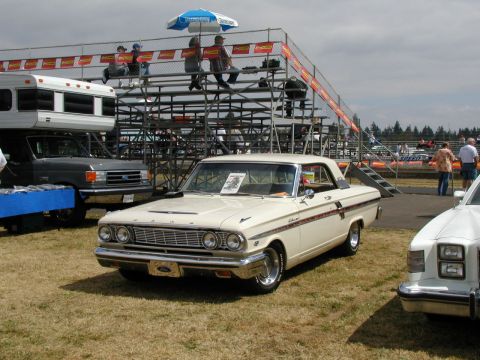 1967 Ford Ranchero - A cream-colored 1964 Ford Falcon two-door hardtop with a red stripe is displayed at a car show, with bleachers and other vehicles in the ba…