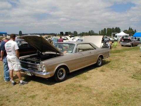 1967 Ford Ranchero - A tan 1967 Ford Galaxie coupe is displayed at a car show with its hood open, alongside other vehicles.