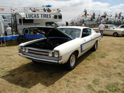 1967 Ford Ranchero - White 1968 Ford Torino GT at an outdoor event, hood up, with RV and bleachers in background.