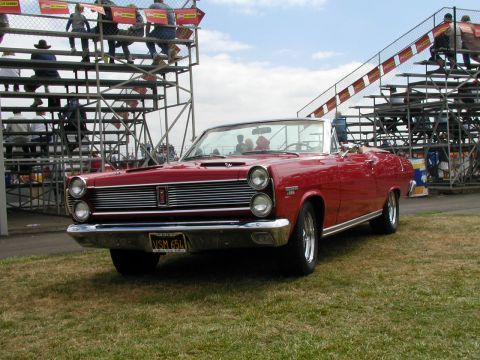 1967 Ford Ranchero - A red 1967 Ford Ranchero convertible is displayed at a car show with spectators in bleachers in the background.