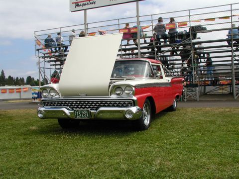1967 Ford Ranchero - A classic red and white pickup truck with its hood open sits on a grassy field before a set of spectator bleachers.