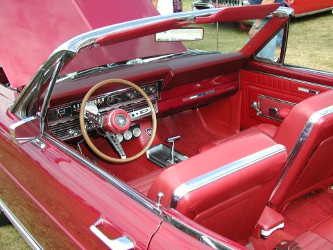 1967 Ford Ranchero - The interior of a classic red convertible is shown, a wooden steering wheel and plush red seating.