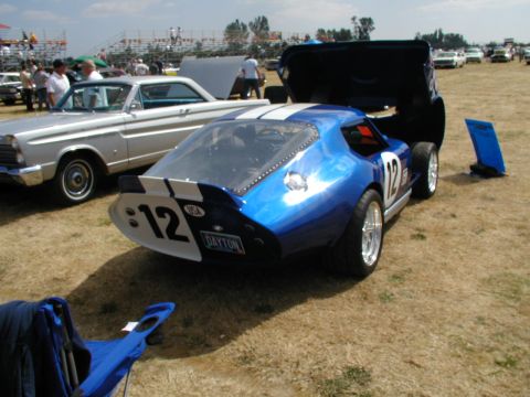 1967 Ford Ranchero - A blue race car with white stripes and the number 12 is parked next to a silver car at an outdoor event.
