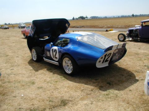 1967 Ford Ranchero - Blue race car with hood open, parked on dry grass next to other vehicles.