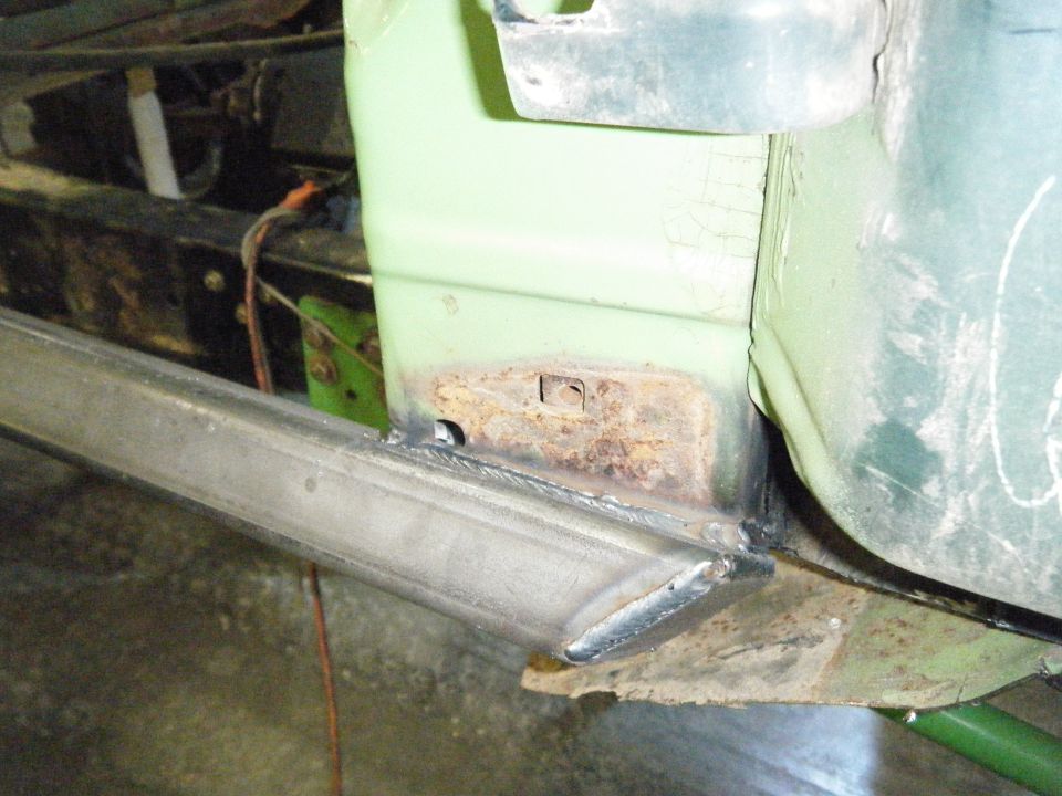 Close-up of rusted metal and fresh welds on a light green vehicle's lower body panel