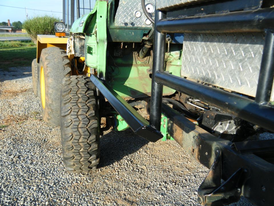 Side view of a modified green truck chassis with large tires and a roll cage