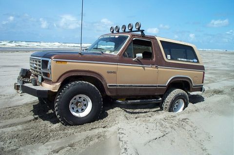 1989 Ford F-150 - This classic Ford Bronco is stuck in the sand on a beach, with the ocean in the background.