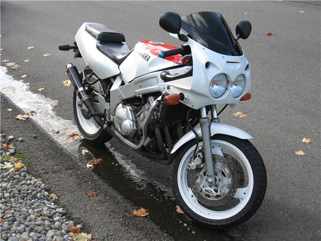 White and red Yamaha sportbike motorcycle with dual round headlights parked on wet pavement