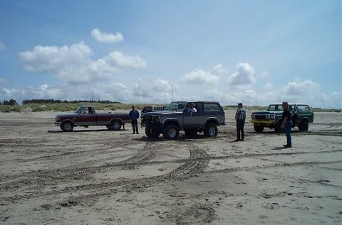 1989 Ford F-150 - A group of trucks and SUVs gathered on a sandy beach under a partly cloudy sky.